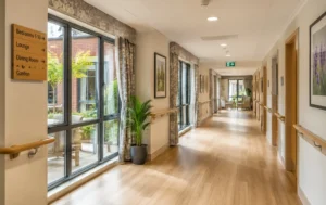 Bright-accessible-care-home-corridor-with-handrails-large-windows-natural-light-modern-flooring-and-clear-wayfinding-signs