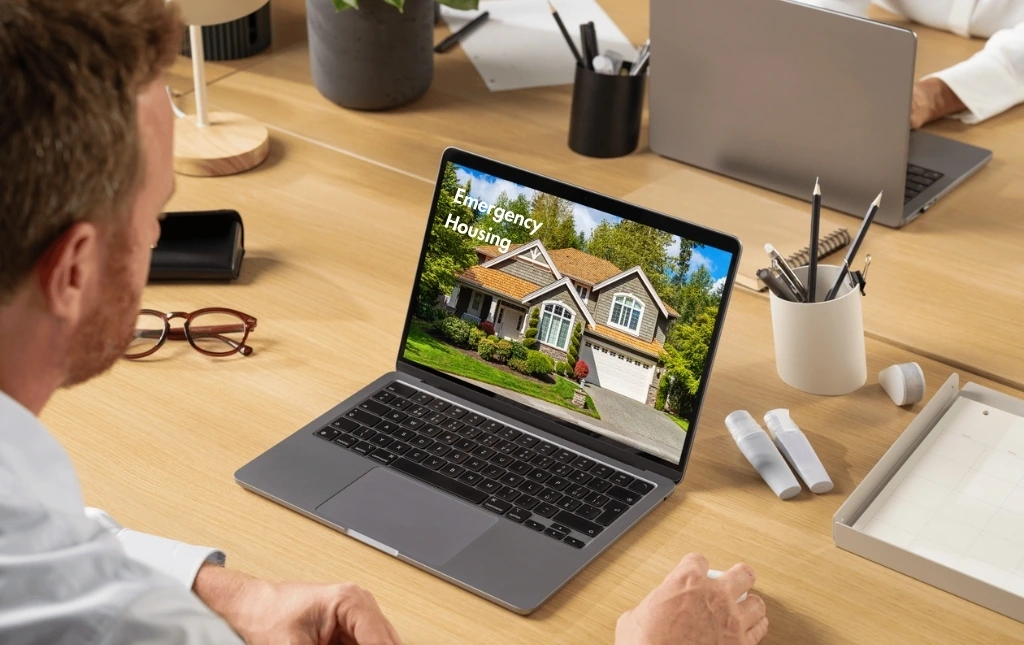 A-person-reviewing-an-emergency-housing-listing-on-a-laptop-screen-surrounded-by-office-supplies