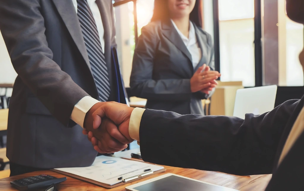 Two-professionals-shaking-hands-in-a-business-setting-while-a-colleague-smiles-in-the-background-representing-along-term-stable-property-partnership-built-on-trust-and-mutual-benefit