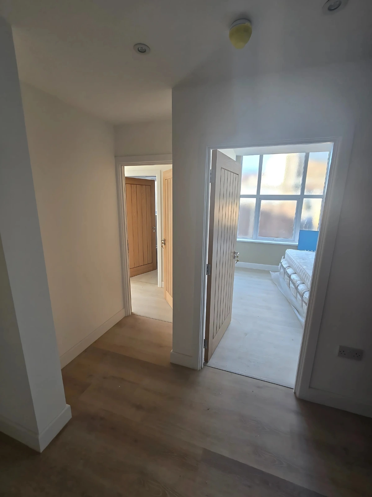 A-hallway-with-two-doors-leading-to-rooms-and-a-view-into-a-bedroom