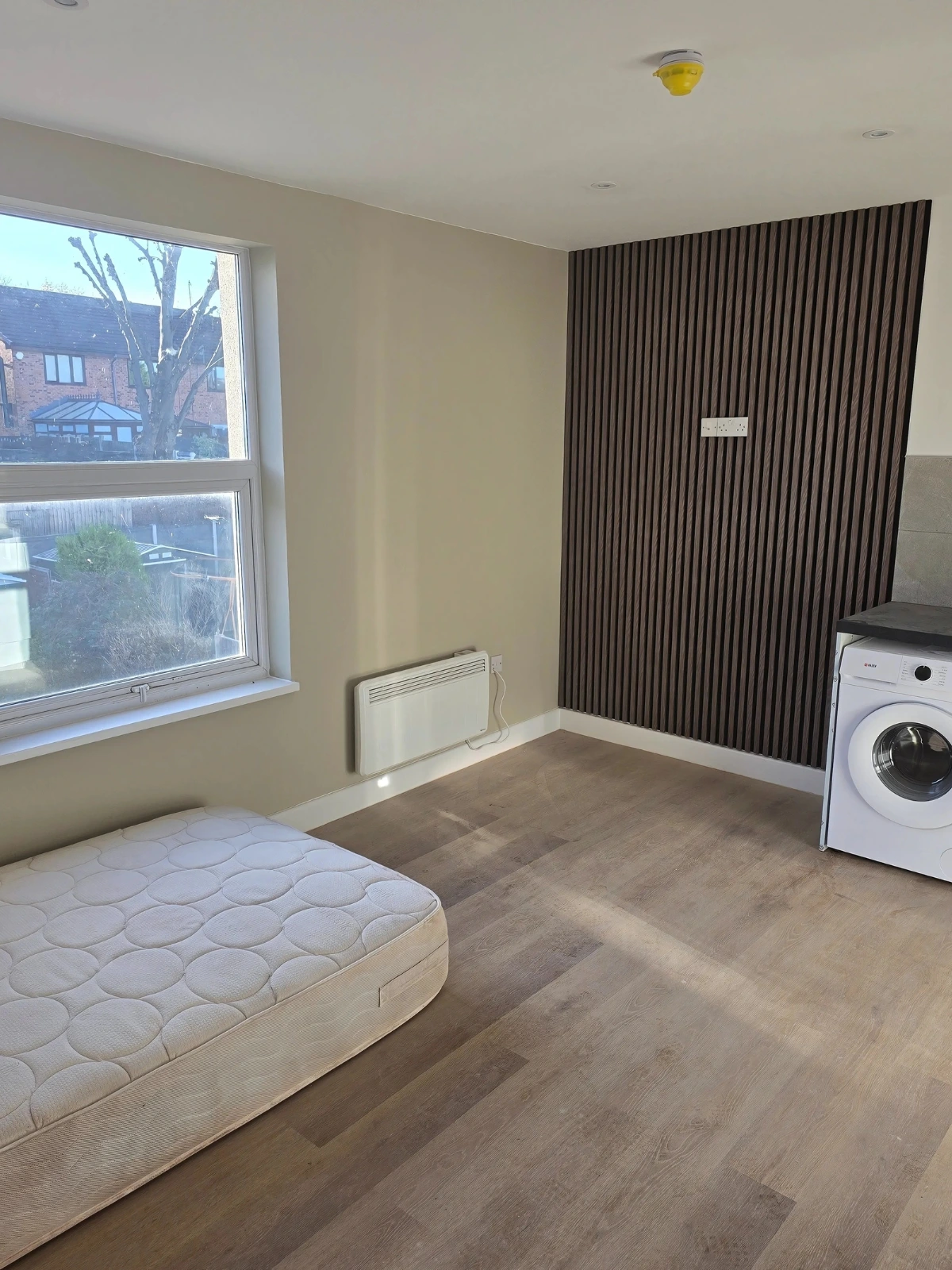 A-partially-furnished-room-with-a-mattress-washing-machine-and-wall-paneling.